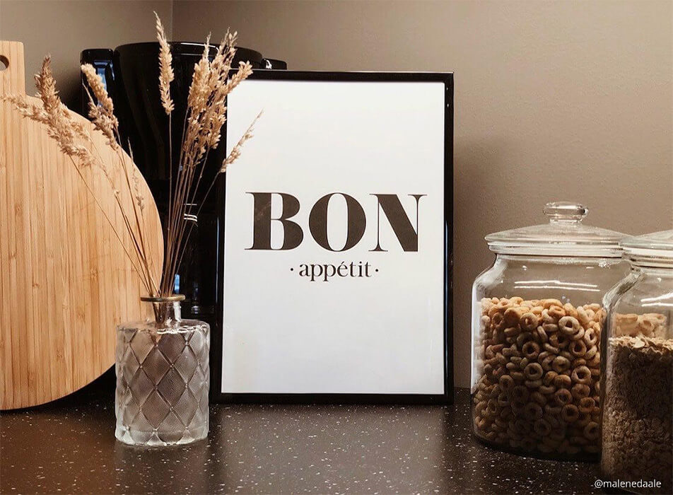 Keukenposter met de tekst Bon appétit, koffiezetapparaat en glazen potten op een donker aanrecht